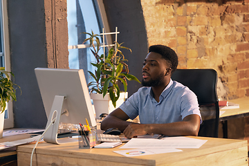 Image showing African businessman, manager working in modern office using devices and gadgets