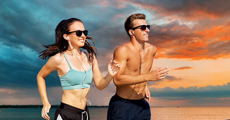 Image showing couple with earphones running along on beach