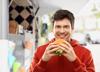 Image showing happy young man eating hamburger at food truck