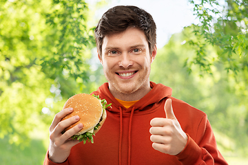 Image showing happy young man with hamburger showing thumbs up