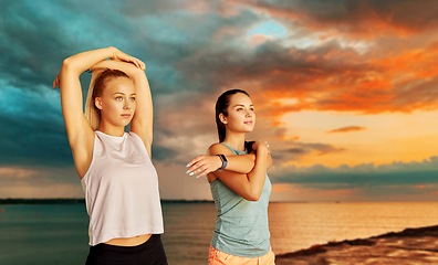 Image showing women with fitness trackers stretching over sea