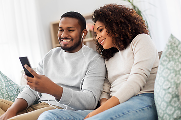 Image showing happy couple with smartphone and earphones at home