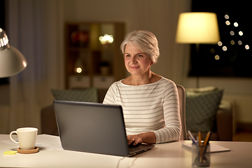 Image showing happy senior woman with laptop at home in evening