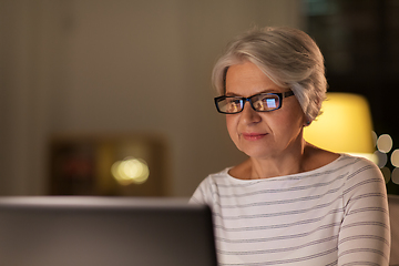 Image showing happy senior woman with laptop at home in evening