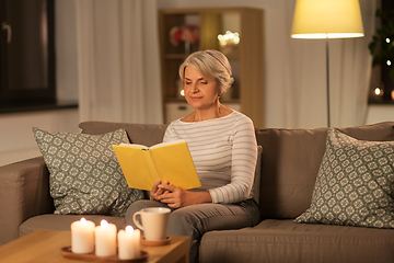 Image showing happy senior woman reading book at home in evening