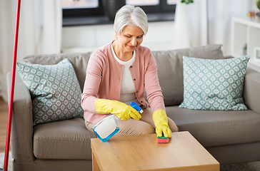 Image showing senior woman with detergent cleaning table at home