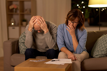 Image showing unhappy senior couple with bills and money at home