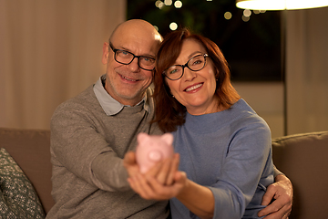 Image showing happy senior couple with piggy bank at home