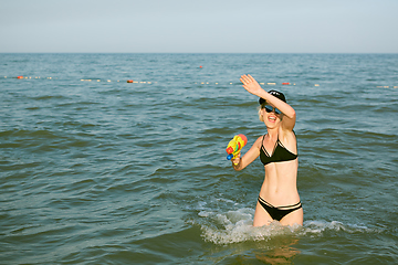 Image showing Happy young woman in a cap with the word queen playing with water gun. Film effect