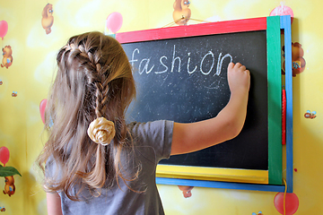 Image showing girl with nice plaits writes word Fashion on blackboard