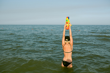 Image showing Happy young woman in a cap with the word queen playing with water gun. Film effect