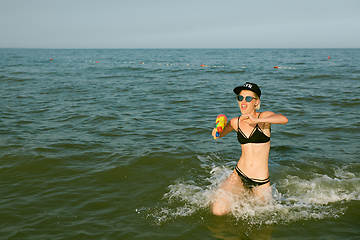 Image showing Happy young woman in a cap with the word queen playing with water gun. Film effect