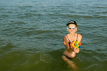 Image showing Happy young woman in a cap with the word queen playing with water gun. Film effect