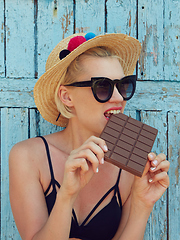 Image showing Young attractive woman in sunglasses and in straw hat eating chocolate on a blue background. Film efect