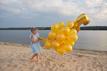 Image showing Little girl with many golden balloons on the beach at sunset