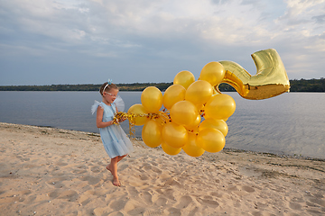 Image showing Little girl with many golden balloons on the beach at sunset