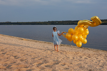 Image showing Little girl with many golden balloons on the beach at sunset