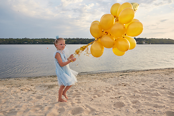 Image showing Little girl with many golden balloons on the beach at sunset