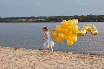 Image showing Little girl with many golden balloons on the beach at sunset