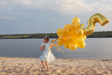 Image showing Little girl with many golden balloons on the beach at sunset