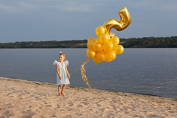 Image showing Little girl with many golden balloons on the beach at sunset