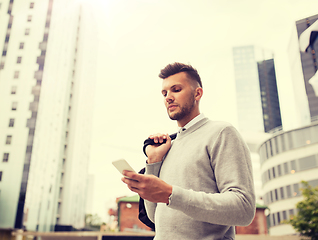 Image showing young man with bag texting on smartphone in city