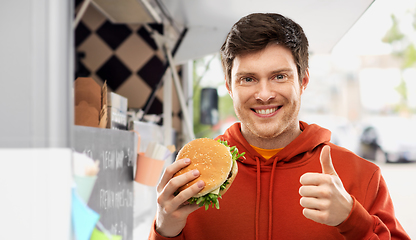 Image showing happy young man with hamburger showing thumbs up