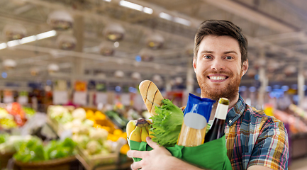 Image showing smiling young man with food in bag at supermarket