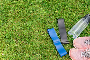 Image showing Ladie's fitness rubber bands and sneakers on the green grass background