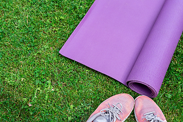 Image showing Ladie's sneakers and fitness mat on the green grass background