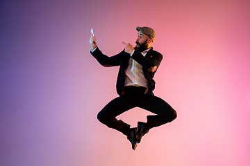 Image showing Full length portrait of happy jumping man in neon light and gradient background