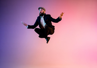 Image showing Full length portrait of happy jumping man in neon light and gradient background