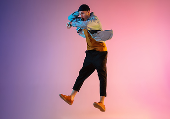 Image showing Full length portrait of happy jumping man in neon light and gradient background