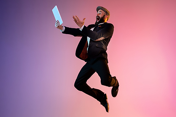 Image showing Full length portrait of happy jumping man in neon light and gradient background