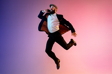 Image showing Full length portrait of happy jumping man in neon light and gradient background
