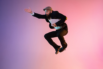 Image showing Full length portrait of happy jumping man in neon light and gradient background