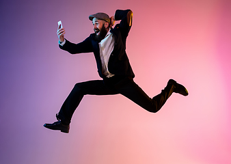 Image showing Full length portrait of happy jumping man in neon light and gradient background