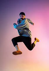 Image showing Full length portrait of happy jumping man in neon light and gradient background