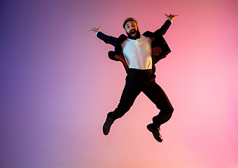 Image showing Full length portrait of happy jumping man in neon light and gradient background