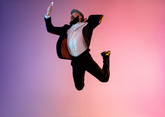 Image showing Full length portrait of happy jumping man in neon light and gradient background