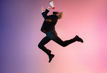 Image showing Full length portrait of happy jumping man in neon light and gradient background