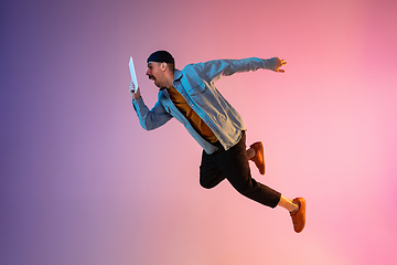 Image showing Full length portrait of happy jumping man in neon light and gradient background