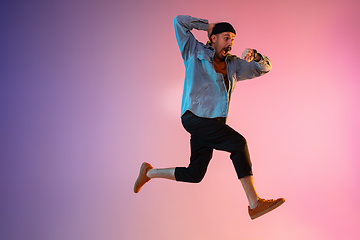 Image showing Full length portrait of happy jumping man in neon light and gradient background