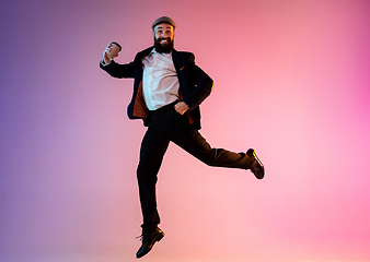 Image showing Full length portrait of happy jumping man in neon light and gradient background