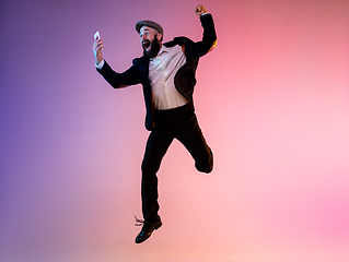 Image showing Full length portrait of happy jumping man in neon light and gradient background