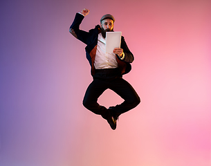 Image showing Full length portrait of happy jumping man in neon light and gradient background