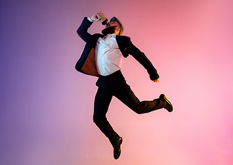 Image showing Full length portrait of happy jumping man in neon light and gradient background