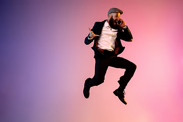 Image showing Full length portrait of happy jumping man in neon light and gradient background