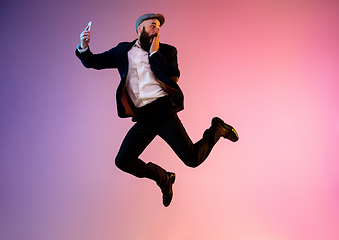 Image showing Full length portrait of happy jumping man in neon light and gradient background