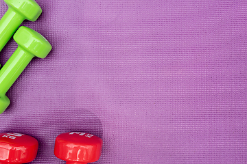 Image showing Ladie's dumbbells over purple fitness mat, top view.